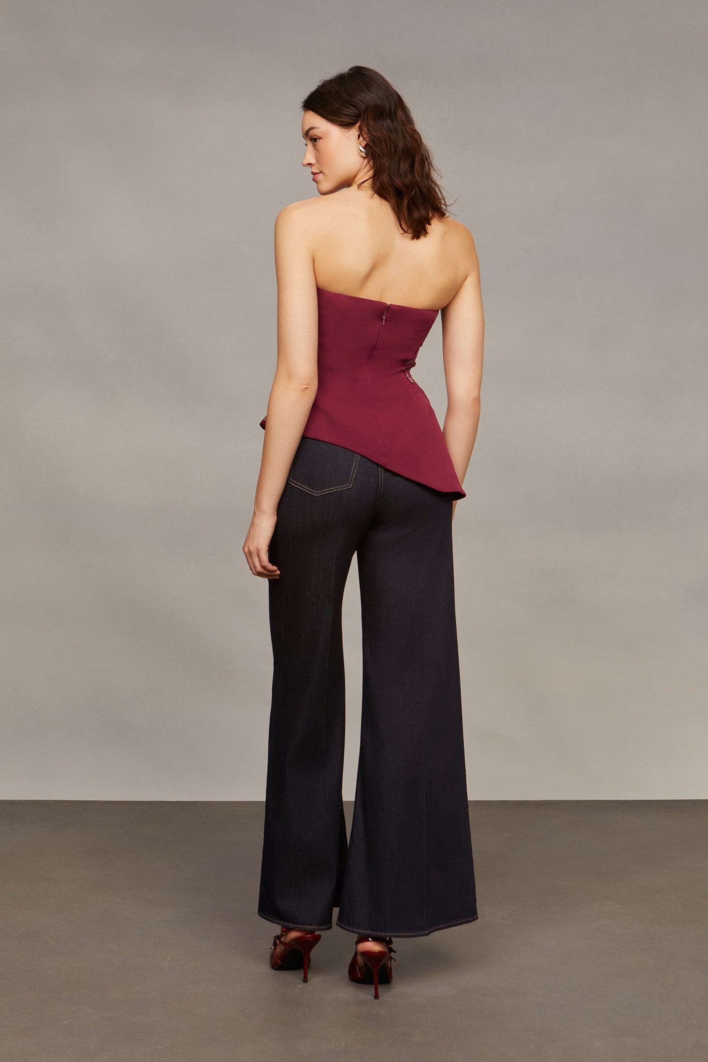 Woman wearing a strapless burgundy top and black flared pants against a plain background
