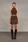 Woman wearing a brown halter top and camouflage skirt with brown knee-high boots against a gray background