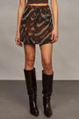 Woman wearing a brown halter top and camouflage skirt with brown knee-high boots against a gray background